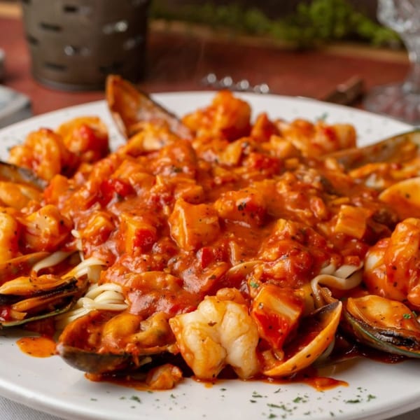Seafood pasta with mussels, shrimp, and clams in a rich red sauce on a white plate.