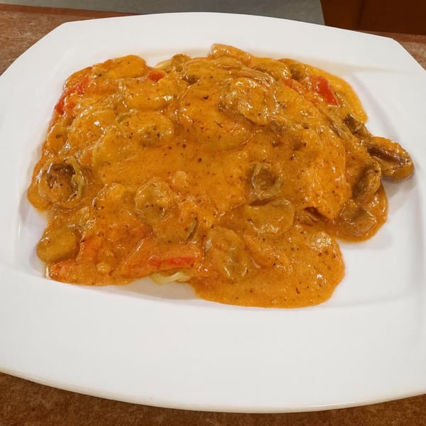 Creamy orange pasta dish with mushrooms and red peppers on a white square plate.